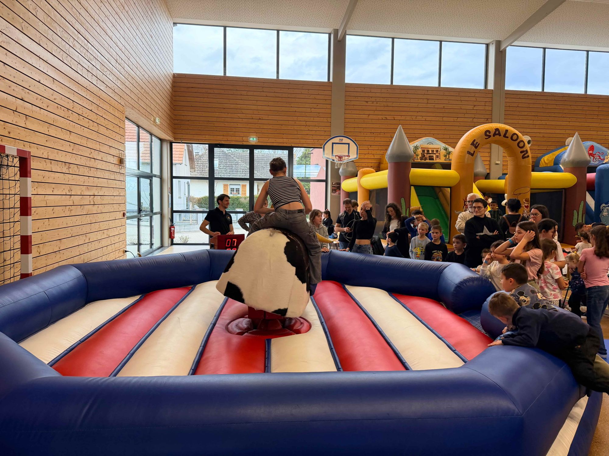 Participant sur un taureau mécanique au centre d'une arène gonflable, devant plusieurs spectateurs