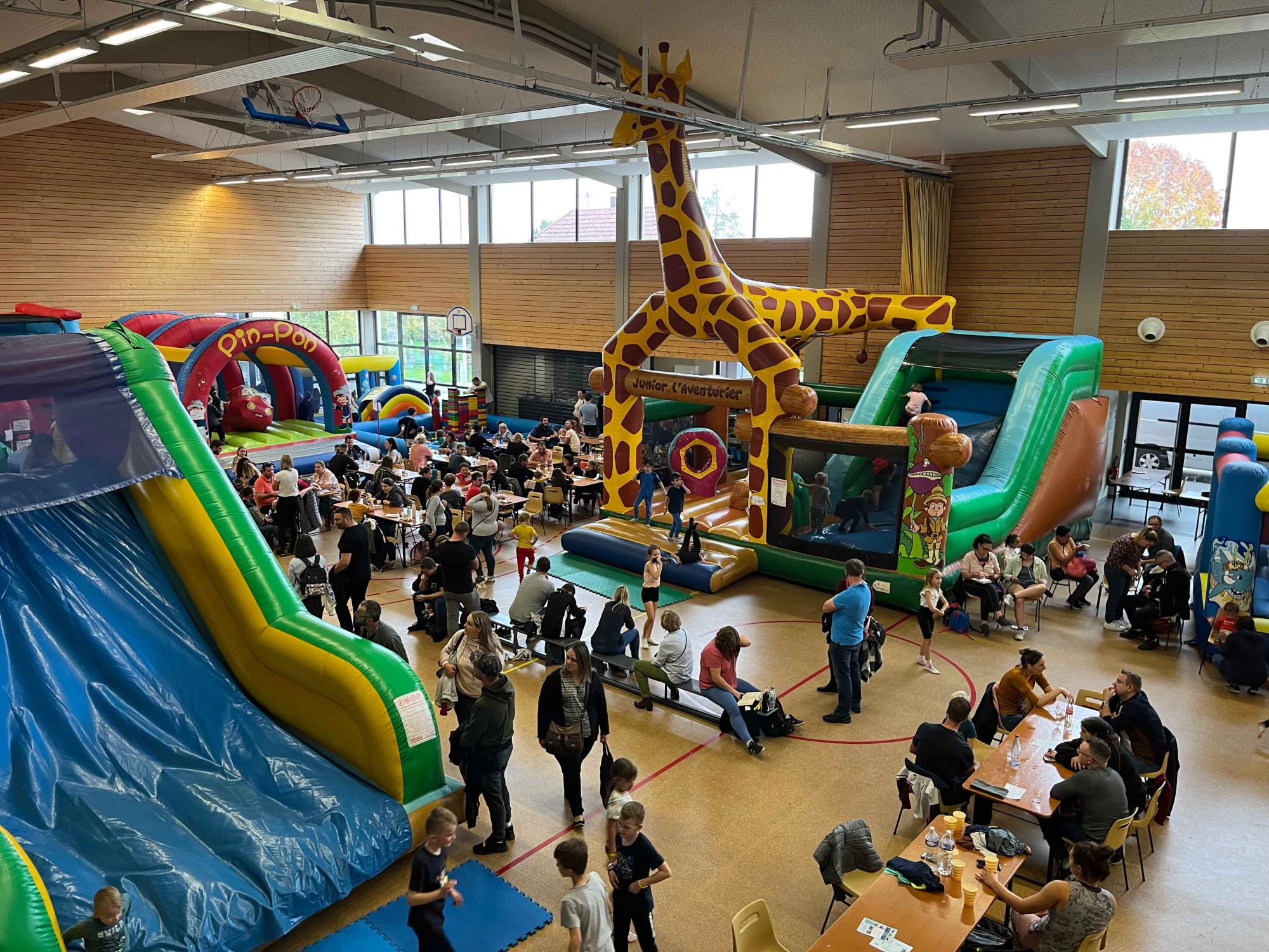 Familles réunies autour des tables et des jeux gonflables avec la grande girafe au centre de la salle