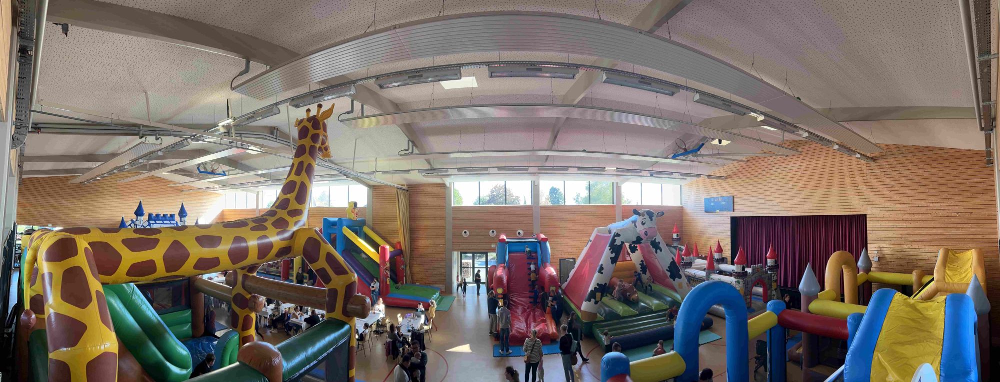 Vue panoramique de la salle polyvalente en 2022 avec la grande girafe gonflable, des châteaux et des toboggans